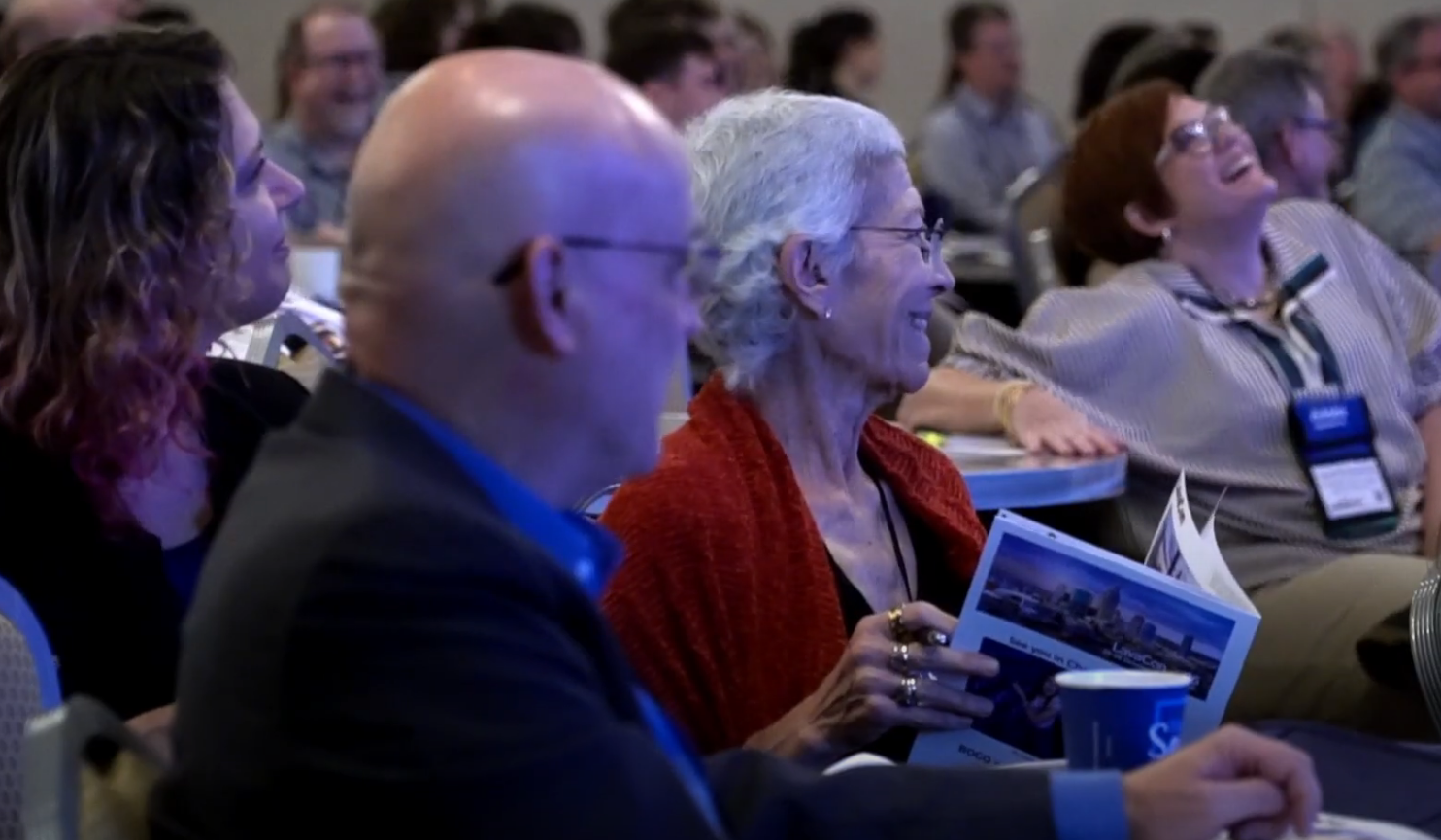People smiling in an audience at a conference